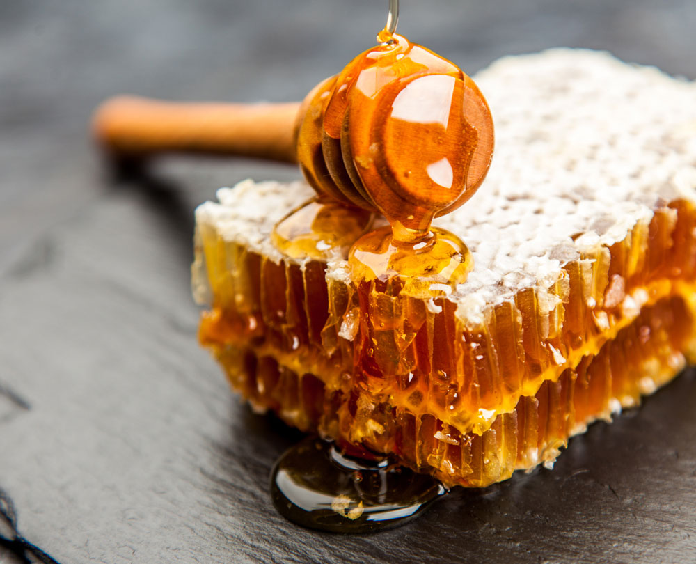 Favo pieno di miele biologico dell'Azienda Agricola I Massi che cola in primo piano con apposito bastoncino dosatore